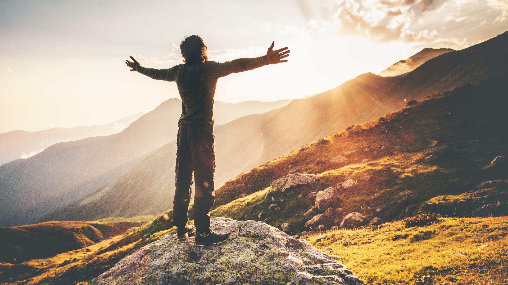 A person stands with open arms in the light above a mountain valley